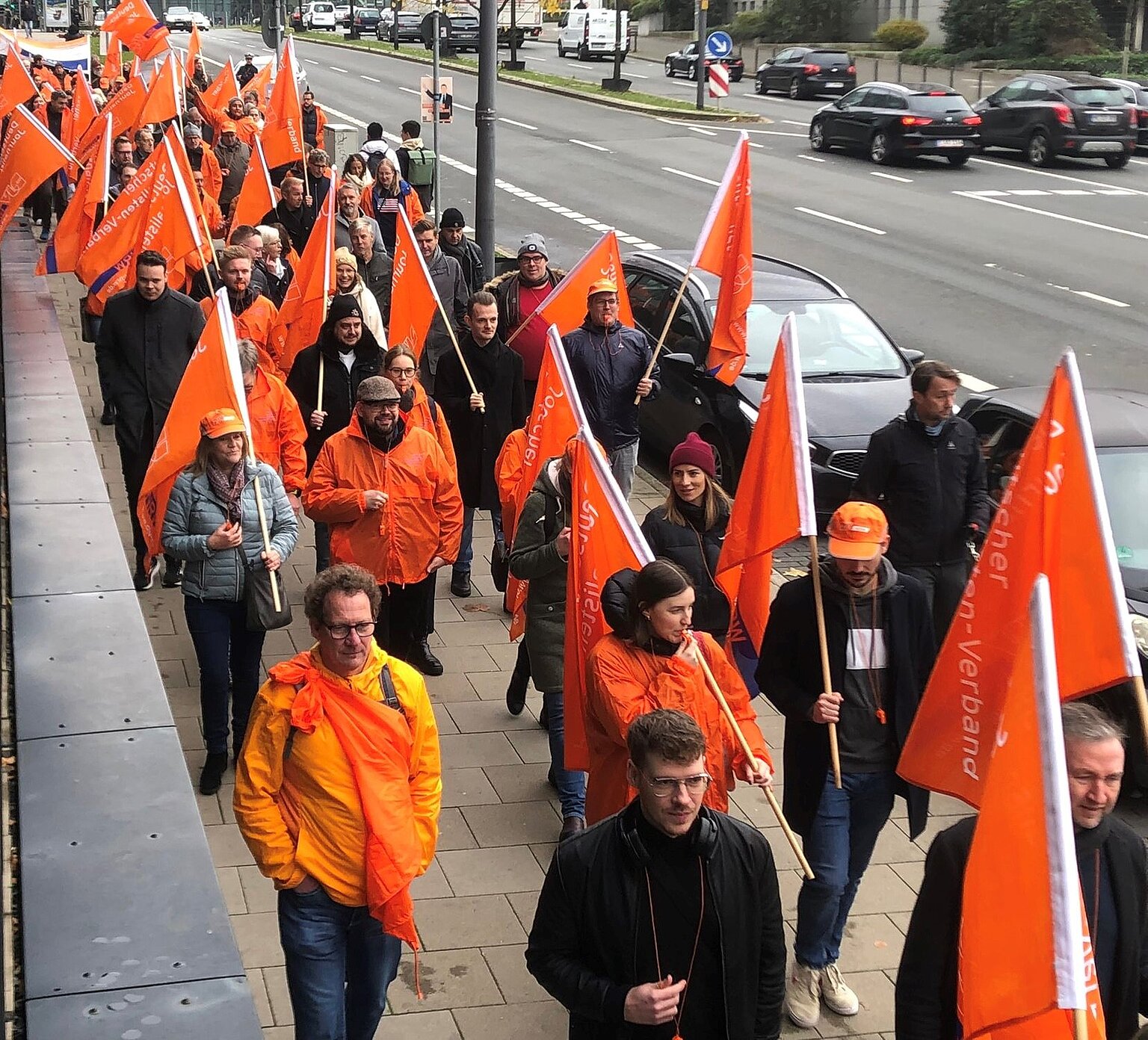 Warnstreik und Demo bei Funke in NRW Ein Streikzug aus Fahnenträgern in orangenen Jacken. – Demonstration vor der Funke-Zentrale in Essen. Foto: Michael Kleinrensing