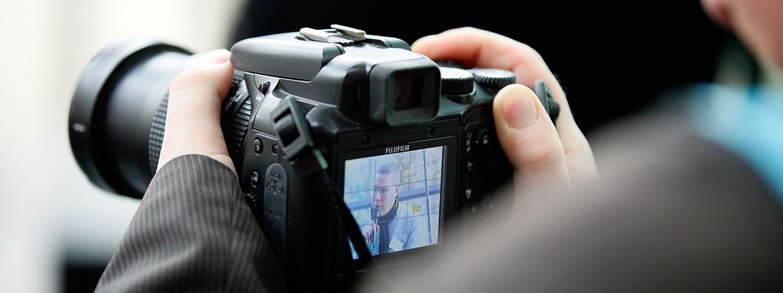 Ein Mann schaut durch den Sucher einer Kamera und drückt den Auslöser.