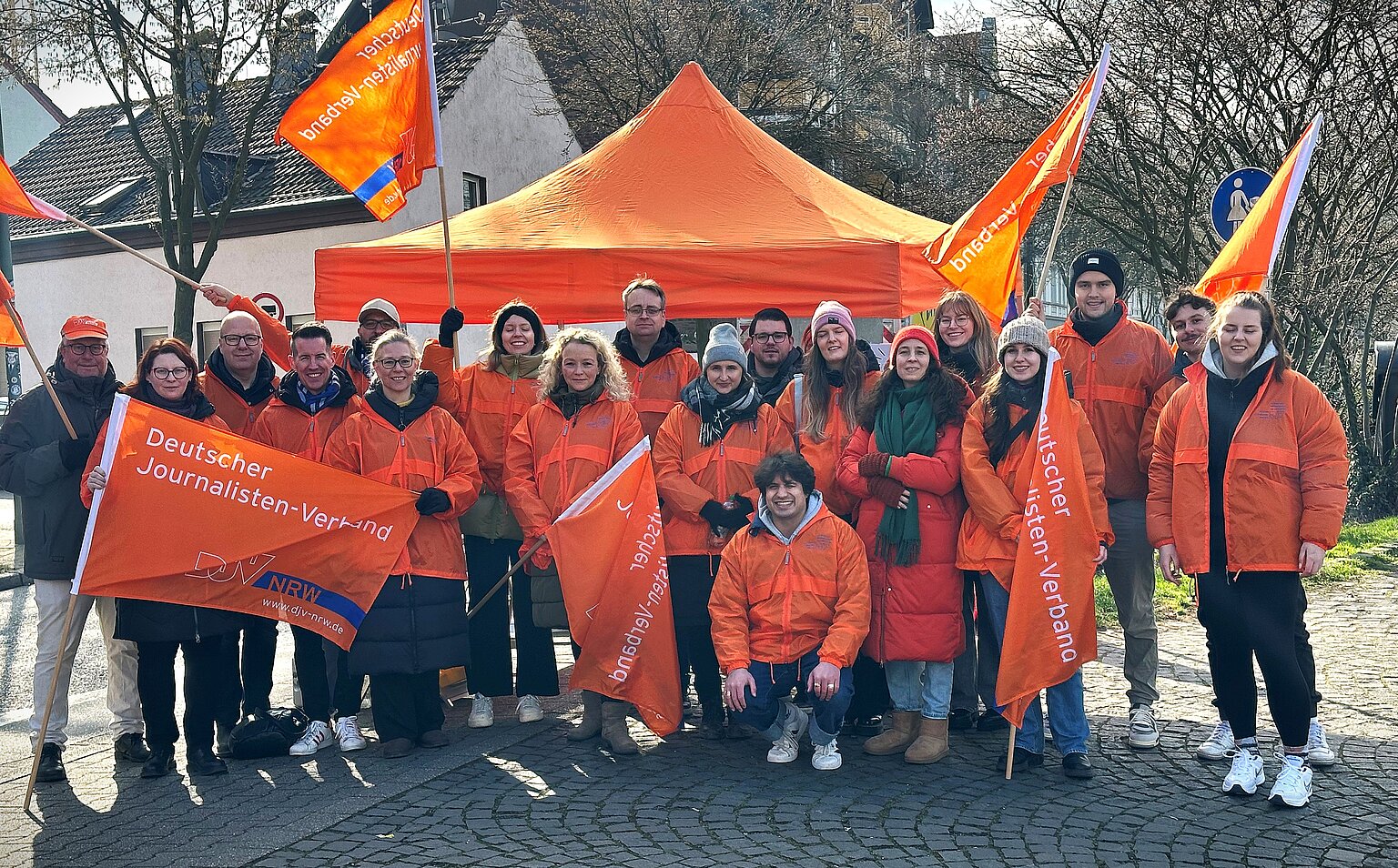 Gruppenbild von einer Protestaktion in Gelsenkirchen. Die Teilnehmenden tragen orangene DJV-Jacken. – 