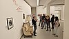 Zur Linken das Loriot-Sofa und an der Wand steht der Name der Ausstellung geschrieben "Ach, was." – 