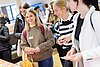 Drei Frauen informieren sich an einem Messestand. – 